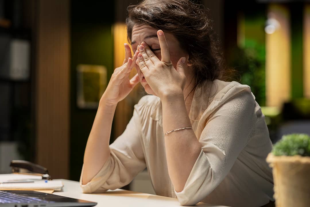 An exhausted professional rubbing her eyes to stay awake after a long work session.